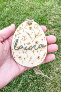 This image shows one of the Easter basket tags made out of wood using an xTool laser machine. It's in the shape of an egg with laser engraved flowers. It has the name Laura on it.