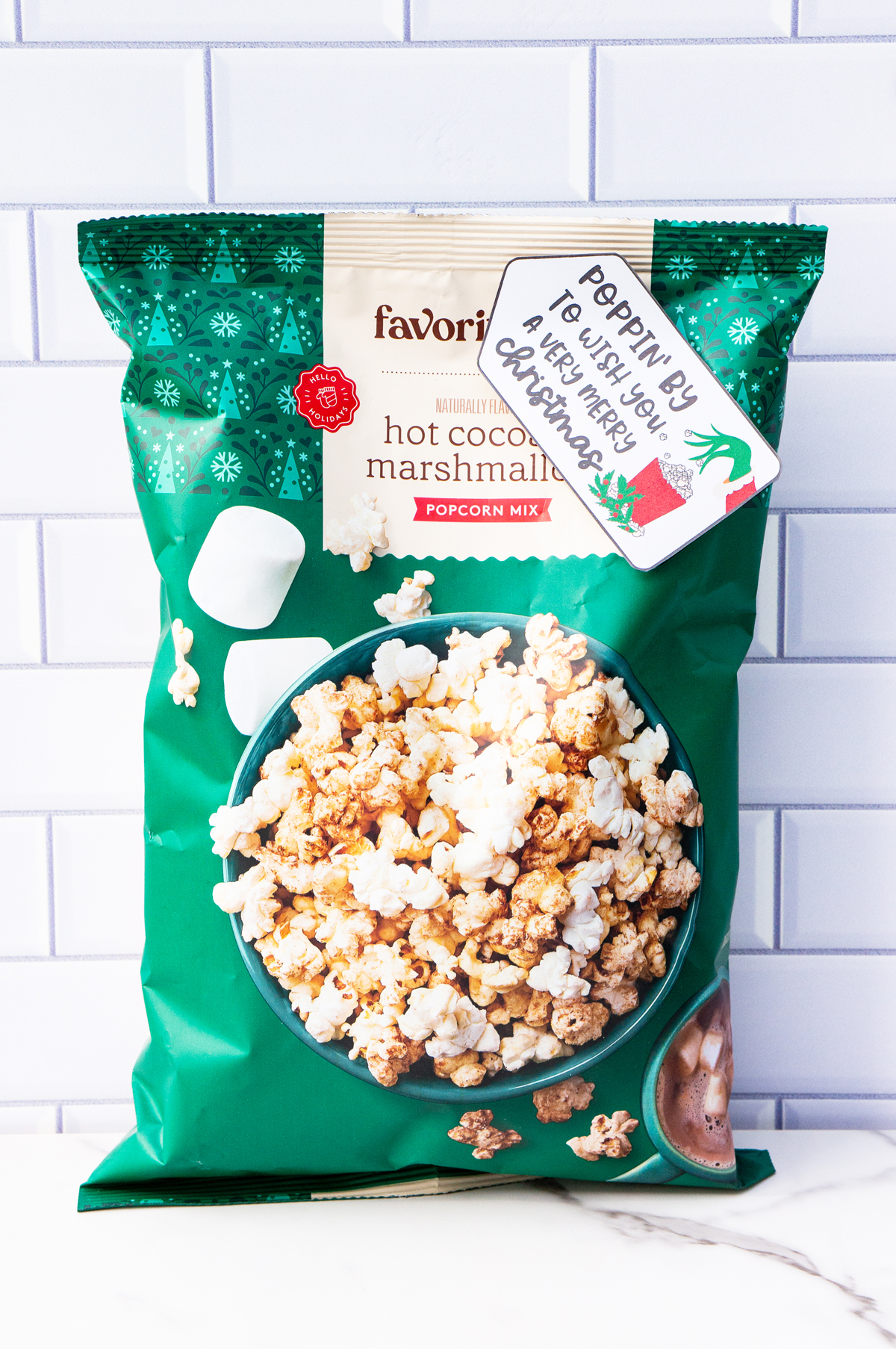 This is one of the free Christmas treat gift tags you can download in this post. It says, Poppin’ By to Wish You a Very Merry Christmas. It has a hand-drawn Grinch hand reaching out stealing popcorn from a red cup of popcorn. The tag is attached to a bag of hot chocolate and marshmallow flavored popcorn.