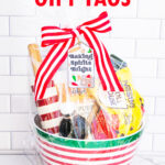 At the top it says free Christmas gift tags and the bottom says 15 unique designs. In-between is an image of one of the free Christmas treat gift tags you can download in this post. It says, Baking Spirits Bright featuring Christmas cookies and baking supplies. It is attached to a gift basket filled with Christmas baking supplies, a Christmas red and white stripped rolling pin, and a red and green spatula.