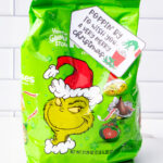 This is one of the free Christmas treat gift tags you can download in this post. It says, Poppin’ By to Wish You a Very Merry Christmas. It has a hand-drawn Grinch hand reaching out stealing popcorn from a red cup of popcorn. The tag is attached to a bag of Grinch themed Hershey Kisses.