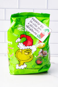 This is one of the free Christmas treat gift tags you can download in this post. It says, Poppin’ By to Wish You a Very Merry Christmas. It has a hand-drawn Grinch hand reaching out stealing popcorn from a red cup of popcorn. The tag is attached to a bag of Grinch themed Hershey Kisses.