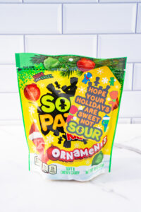 This is one of the free Christmas treat gift tags you can download in this post. It says, Hope Your Holidays are Sweet Not Sour. This Sour Patch Kids-themed tag features hand-drawn Sour Patch kids wearing some snow gear and having a snowball fight. The tag is attached to a bag of Sour Patch Kids ornaments candy.