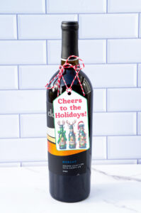 This is one of the free Christmas treat gift tags you can download in this post. It says, Cheers to the Holidays. It features bottles of beer decorated with Christmas lights, antlers, and one has a Santa hat. The tag is attached to a bottle of wine.