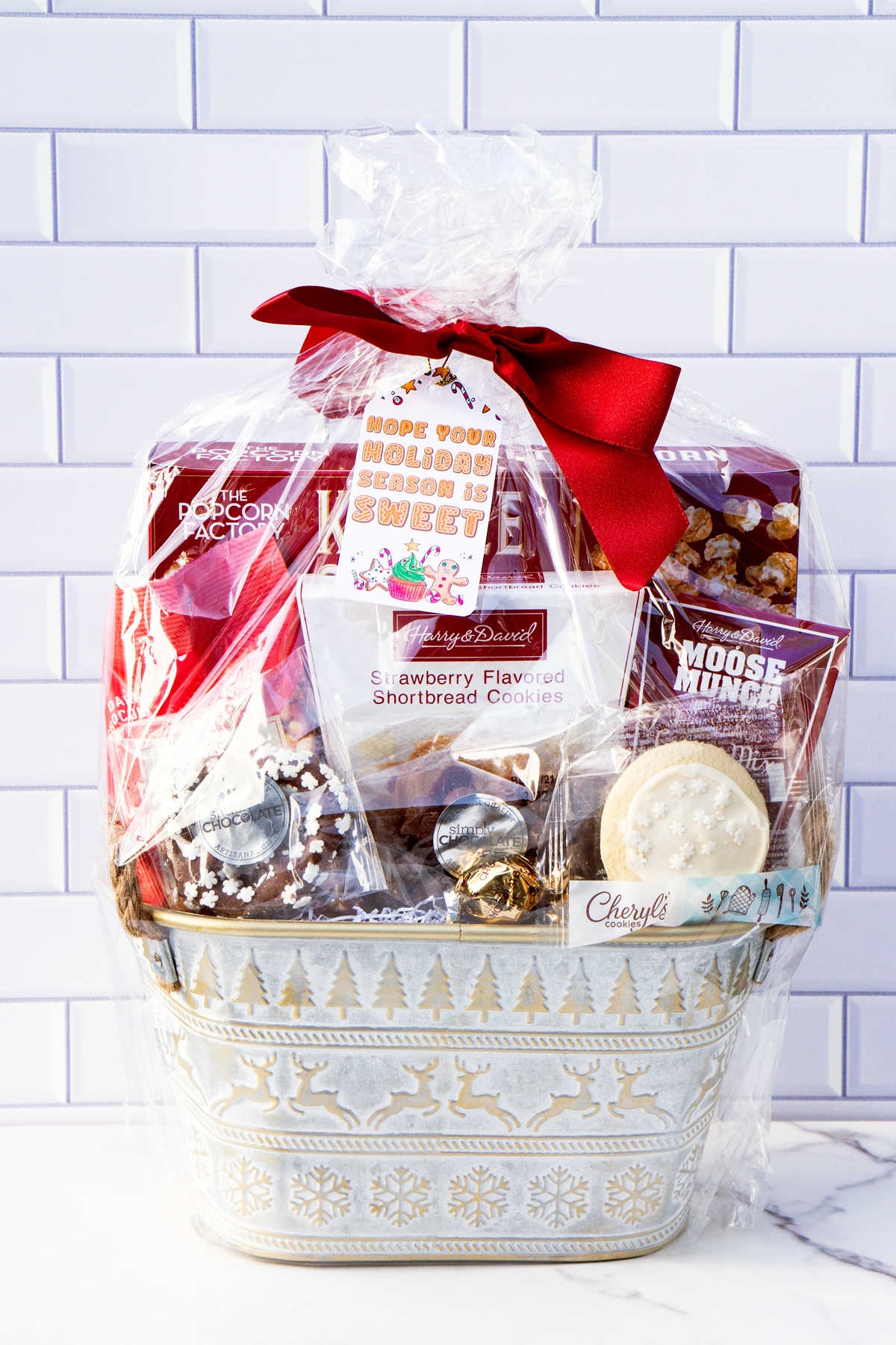 This is one of the free Christmas treat gift tags you can download in this post. It says, Hope Your Holiday Season is Sweet. This fag features a gingerbread man and other sweet Christmas treats. The tag is attached to a gift basket filled with holiday treats.