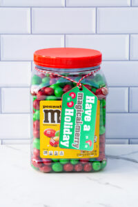 This is one of the free Christmas treat gift tags you can download in this post. It says, Have a Magical & Merry Holiday. It features hand-drawn red and green M&M candies. The tag is attached to a container of Peanut M & Ms.