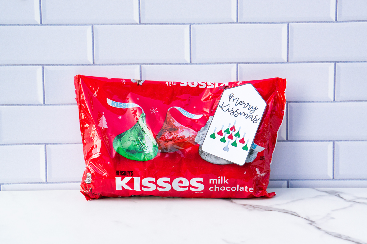 This is one of the free Christmas treat gift tags you can download in this post. It says, Merry Kissmas and featuring Hershey Kisses in their iconic Christmas design in the shape of a bell. The tag is attached to a bag of Hershey kisses.