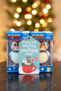 This is one of the free Christmas treat gift tags you can download in this post. It says, You’re Worth Melting For. It features a marshmallow snowman soaking in hot cocoa in a mug with some cookies and treats surrounding the mug. The tag is attached to a box of hot chocolate chocolate bombs.