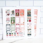 Close-up of three printed book-themed planner sticker sheets propped upright against white subway-tile, showing reading quotes, functional boxes, and decorative illustrations.