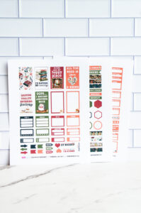 Close-up of three printed book-themed planner sticker sheets propped upright against white subway-tile, showing reading quotes, functional boxes, and decorative illustrations.
