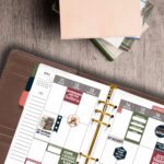 Flat lay of an open planner decorated with book-themed stickers next to a stack of hardcover books on a wooden surface.