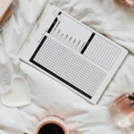 Dream tracker printable styled on a white bedspread alongside roses, a pink mug with a gold spoon, a notebook, and a perfume bottle.