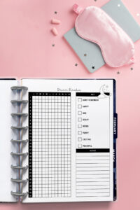 Dream tracker inserted into a discbound planner, photographed on a pink background with a sleep mask, earplugs, and scattered star confetti.