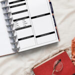 Dream log page inside a discbound planner laid open on a cozy bed, surrounded by a knitted blanket, a red journal with glasses resting on top, and warm-toned fabrics for a soft, relaxed morning vibe.