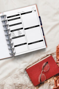 Dream log page inside a discbound planner laid open on a cozy bed, surrounded by a knitted blanket, a red journal with glasses resting on top, and warm-toned fabrics for a soft, relaxed morning vibe.