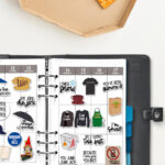 Open planner with Gilmore Girls&ndash;themed stickers arranged in the weekly layout, shown beside a pizza box with a partially eaten slice on a white table.