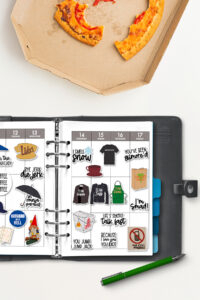 Open planner with Gilmore Girls&ndash;themed stickers arranged in the weekly layout, shown beside a pizza box with a partially eaten slice on a white table.
