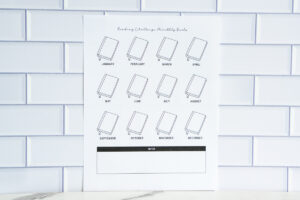 A printable &ldquo;Reading Challenge: Monthly Goals&rdquo; tracker featuring twelve outlined book icons labeled January through December, with a notes section at the bottom, displayed against a white subway tile background.