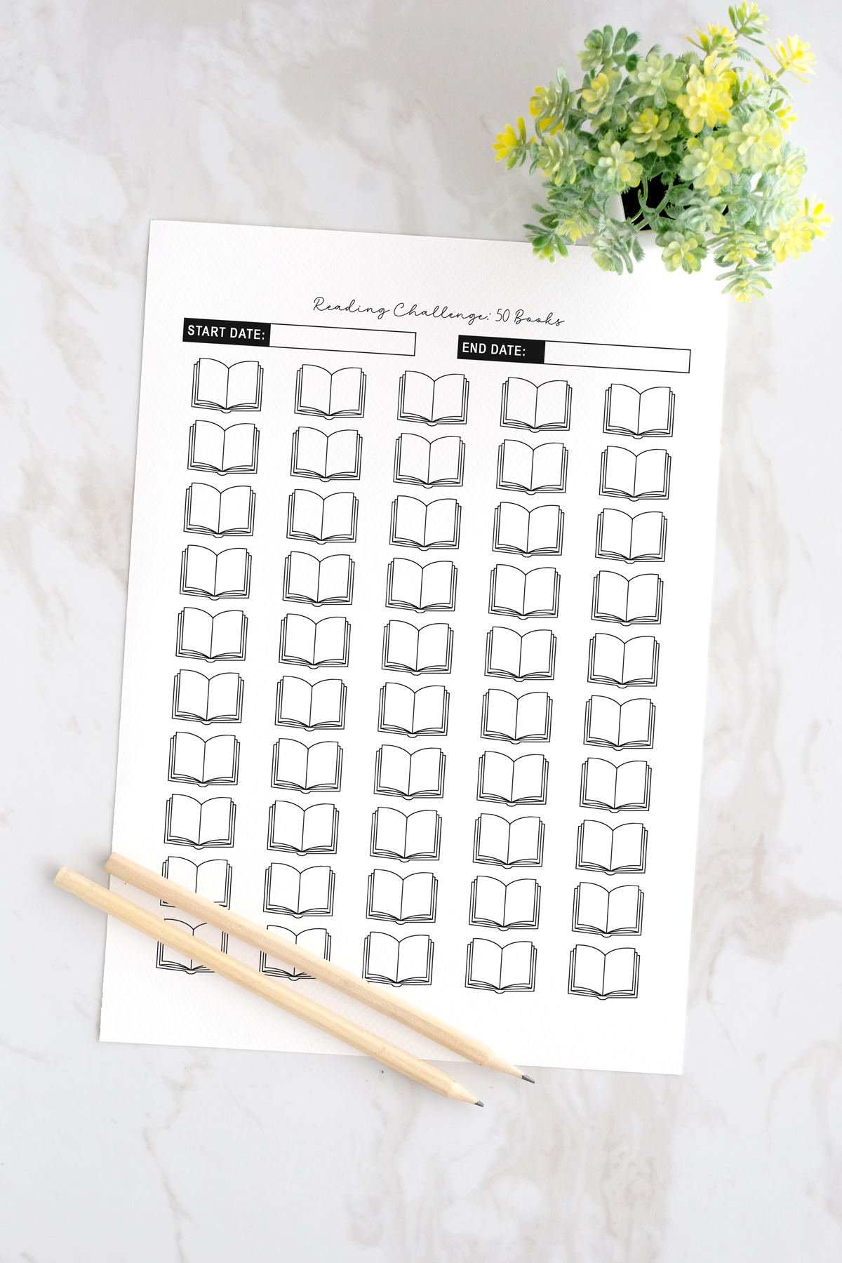 Printed 50 Books Reading Challenge tracker page displayed on a marble surface with two wooden pencils and a small potted plant, featuring rows of open book icons and spaces for start and end dates.