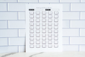A wide image of a &ldquo;Reading Challenge: 50 Books&rdquo; printable sheet with rows of open-book icons and start/end date boxes, positioned against a white tile background.