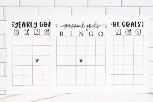 Three printable bingo sheets&mdash;Yearly Goals Bingo, Personal Goals Bingo, and School Goals Bingo&mdash;arranged side by side against a white subway tile background, each showing a blank grid with a star in the center of the first two pages.