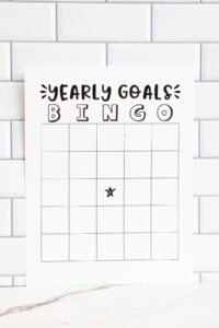 A &ldquo;Yearly Goals Bingo&rdquo; printable page displayed against a white subway tile background, featuring a blank bingo grid with a centered star icon.