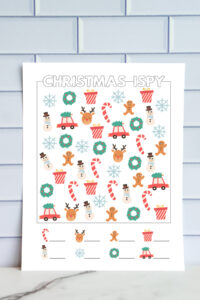 Printed full-color easy Christmas I-Spy worksheet featuring large, simple holiday icons including reindeer, wreaths, gingerbread men, presents, snowflakes, snowmen, candy canes, and cars with Christmas trees. Blank lines at the bottom for kids to record their counts.