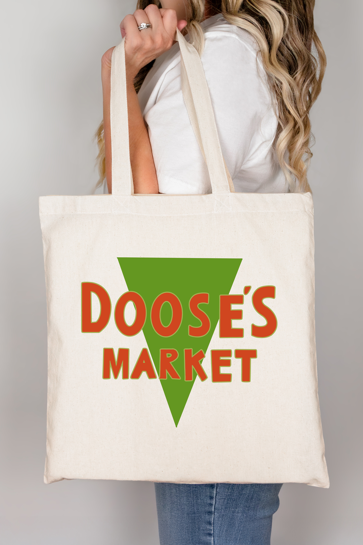 Close-up side view of a cream tote bag displaying the green triangle and orange “Doose’s Market” logo.