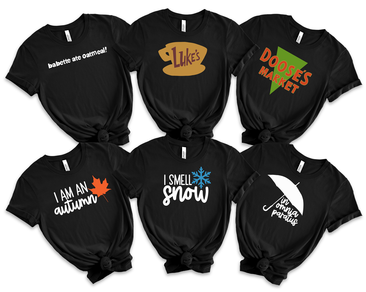 Flat lay of six black T-shirts featuring Gilmore Girls–inspired SVG designs, including Babette Ate Oatmeal, Luke’s logo, Doose’s Market, I Am an Autumn, I Smell Snow, and In Omnia Paratus.