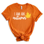 Orange T-shirt with the phrase “I am an autumn” in white script paired with a yellow maple leaf graphic.