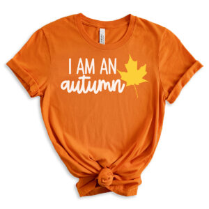 Orange T-shirt with the phrase &ldquo;I am an autumn&rdquo; in white script paired with a yellow maple leaf graphic.