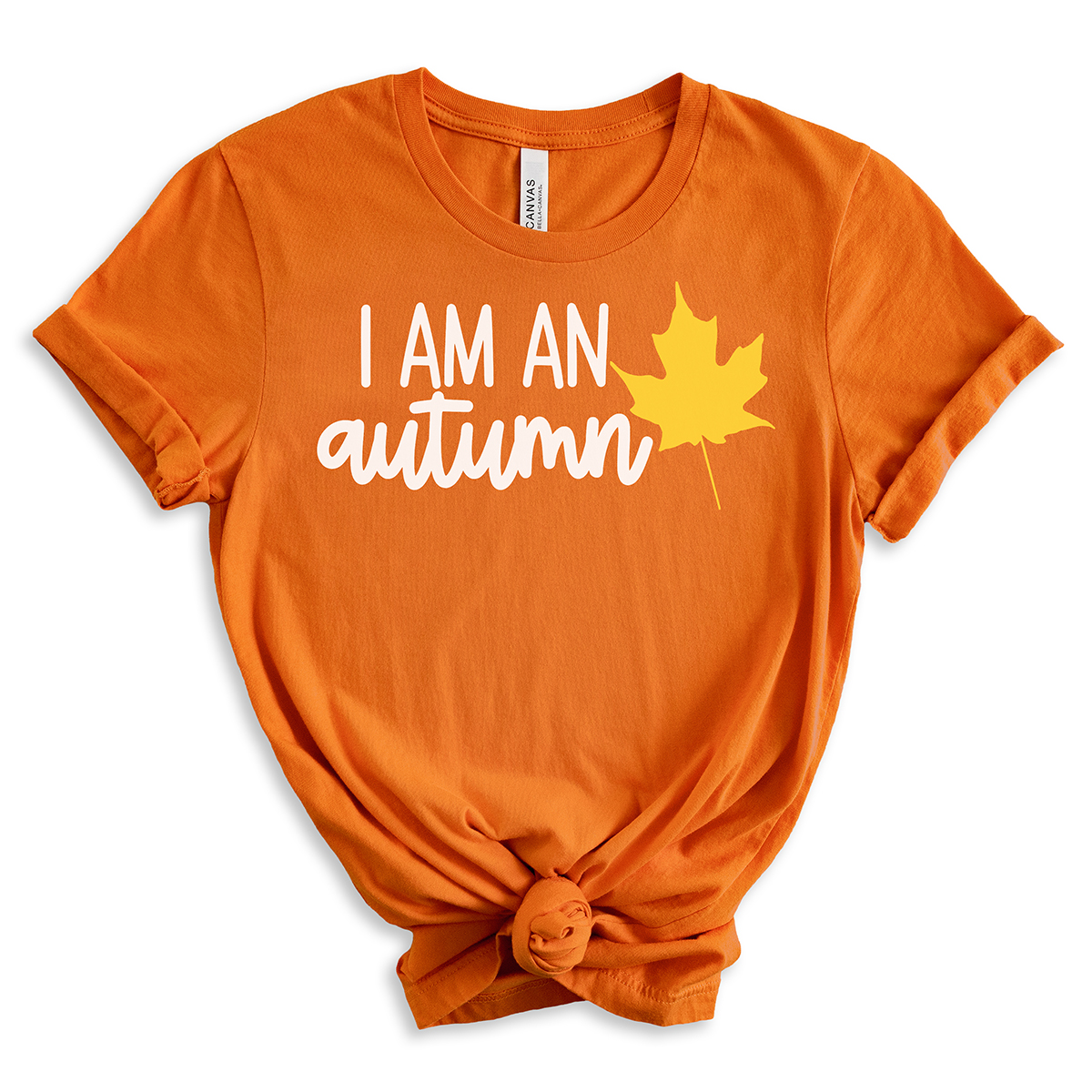 Orange T-shirt with the phrase “I am an autumn” in white script paired with a yellow maple leaf graphic.