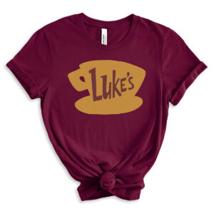 Burgundy t-shirt featuring a large golden coffee cup graphic with the word &ldquo;Luke&rsquo;s&rdquo; in brown, inspired by the Gilmore Girls diner logo, styled with rolled sleeves and a front knot.