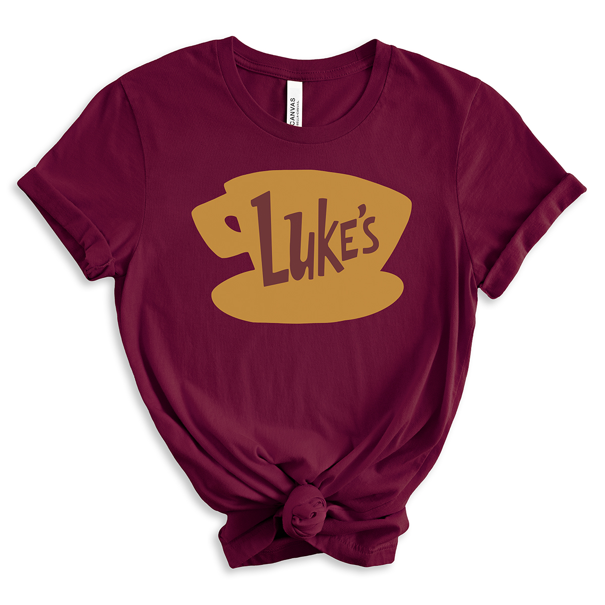 Burgundy t-shirt featuring a large golden coffee cup graphic with the word “Luke’s” in brown, inspired by the Gilmore Girls diner logo, styled with rolled sleeves and a front knot.