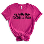 Bright pink t-shirt with the phrase “oy with the POODLES ALREADY” in black lettering, styled with rolled sleeves and a front knot.