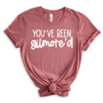 Mauve-pink t-shirt with the phrase “You’ve been Gilmore’d” in white lettering, styled with rolled sleeves and a front knot.