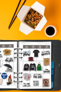 Planner open to a weekly spread decorated with Gilmore Girls stickers, placed on an orange background next to an open takeout container of rice, chopsticks, and a small cup of soy sauce.