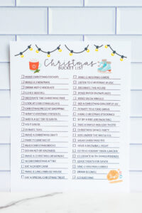 Christmas bucket list printable with illustrated string lights, a hot cocoa mug, and ice skates, shown against a white tile background. The list includes festive activities with checkboxes.