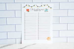 Two-column Christmas bucket list printable with empty checkboxes and festive illustrations, photographed against a tile backdrop.