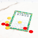 One black-and-white bingo sheet and two full-color Super Bowl Bingo sheets displayed side by side against a white subway tile backdrop.
