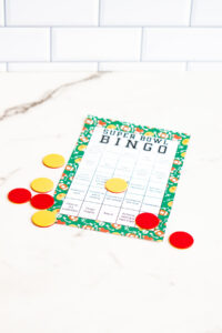 One black-and-white bingo sheet and two full-color Super Bowl Bingo sheets displayed side by side against a white subway tile backdrop.