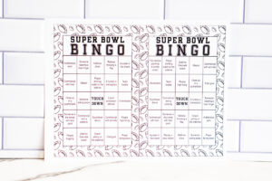 Two black-and-white Super Bowl Bingo sheets shown side by side against a white subway tile backdrop.