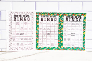 Super Bowl Bingo card with a green illustrated border displayed on a white surface with red and yellow bingo markers around it.
