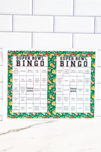 Two bright green Super Bowl Bingo sheets displayed together against a white subway tile wall.
