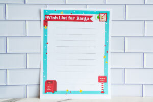 Printable Wish List for Santa page with a turquoise border, red banner title, lined writing space, and festive graphics including a red mailbox and North Pole sign displayed against a white tile background.