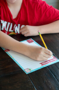 Child writing on a colorful Dear Santa letter printable with a pencil at a wooden table.