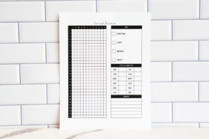 Printed yearly period tracker page displayed against a white subway tile backdrop. The page includes a vertical 31-day grid labeled with months, a symptom key for spotting through heavy flow, a cycle length chart for each month, and a lined notes section.
