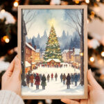 Person holding a framed vintage-style print of a snowy town square with a large lit Christmas tree and people gathered around, with a blurred Christmas tree in the background.