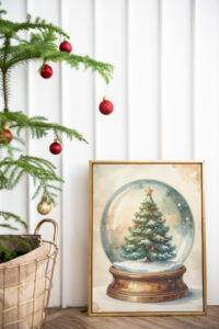Framed vintage-style snow globe Christmas print placed on the floor next to a small tree decorated with red and gold ornaments.