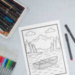 Relaxation coloring page featuring a mountain lake with pine trees and a rowboat, surrounded by colored pencils and markers on a tabletop.