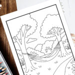 Relaxation coloring page of a peaceful hammock tied between two trees in a quiet forest setting, shown on a wooden table with colored pencils nearby.